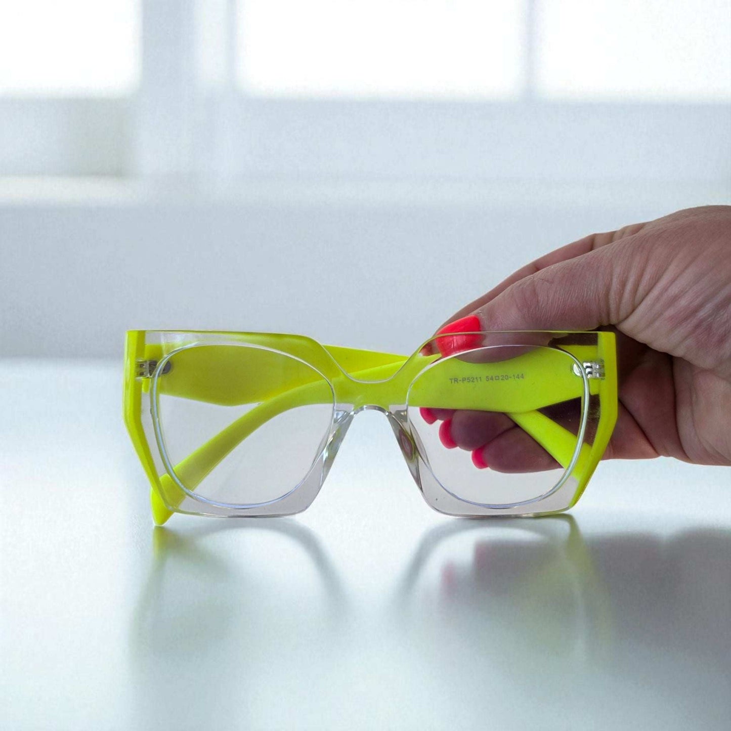 Neon Yellow Reading Glasses with blue light filter and lightweight frame held by hand against bright background