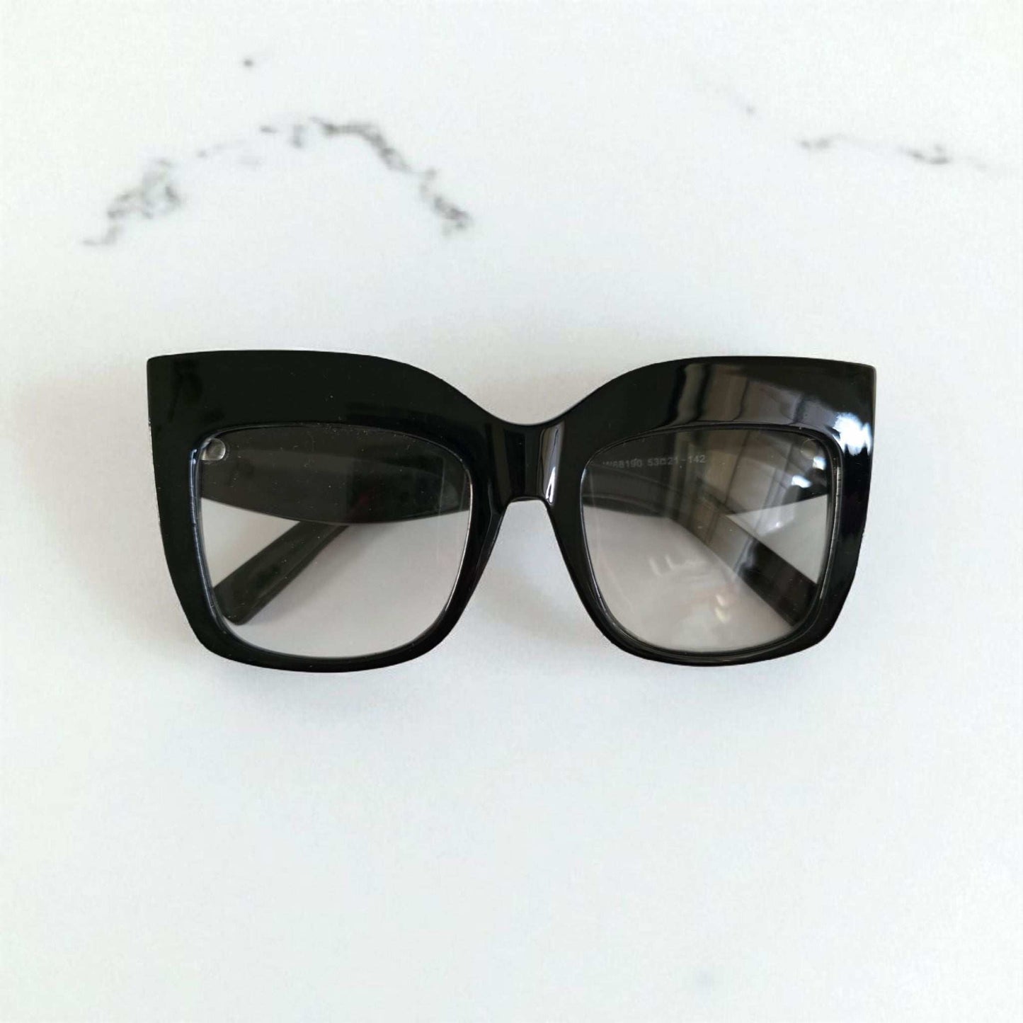Black oversized cat eye reading glasses with thick glossy frames and slightly tinted lenses.