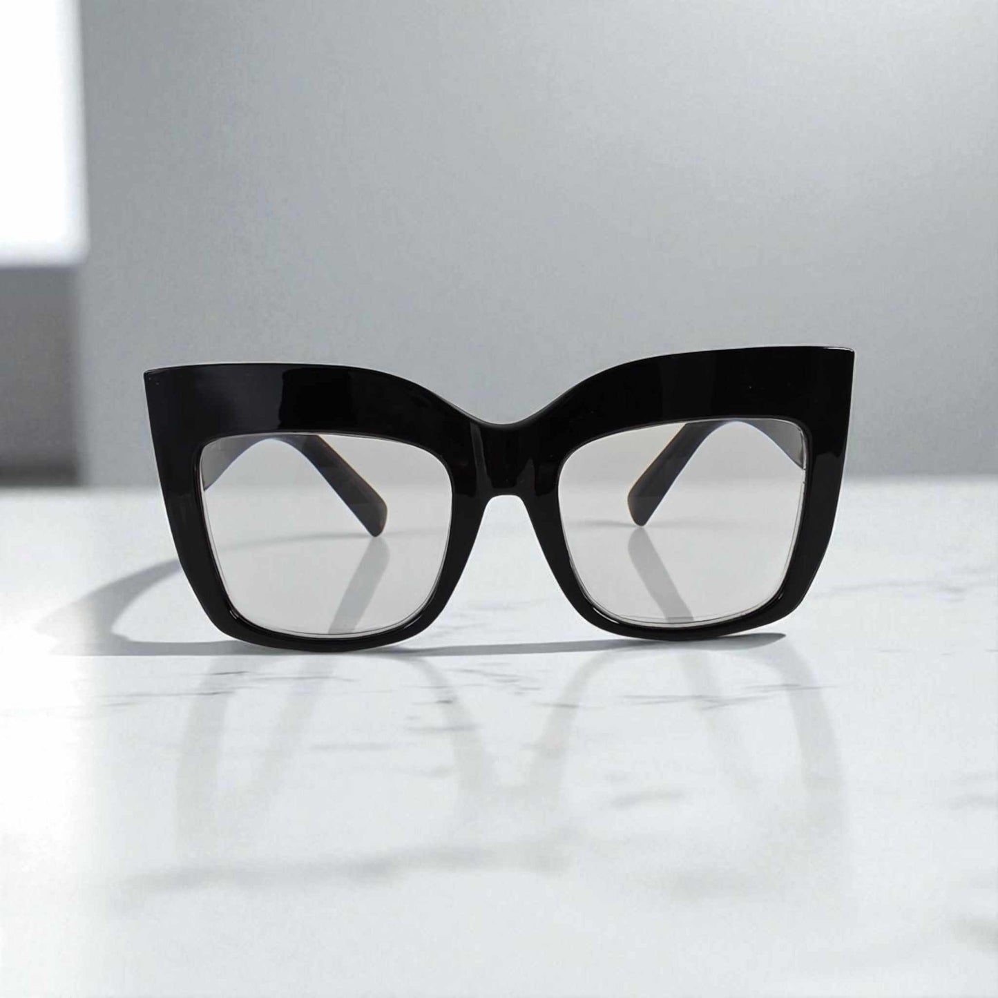 Black oversized cat eye reading glasses with blue light filter lenses on white surface