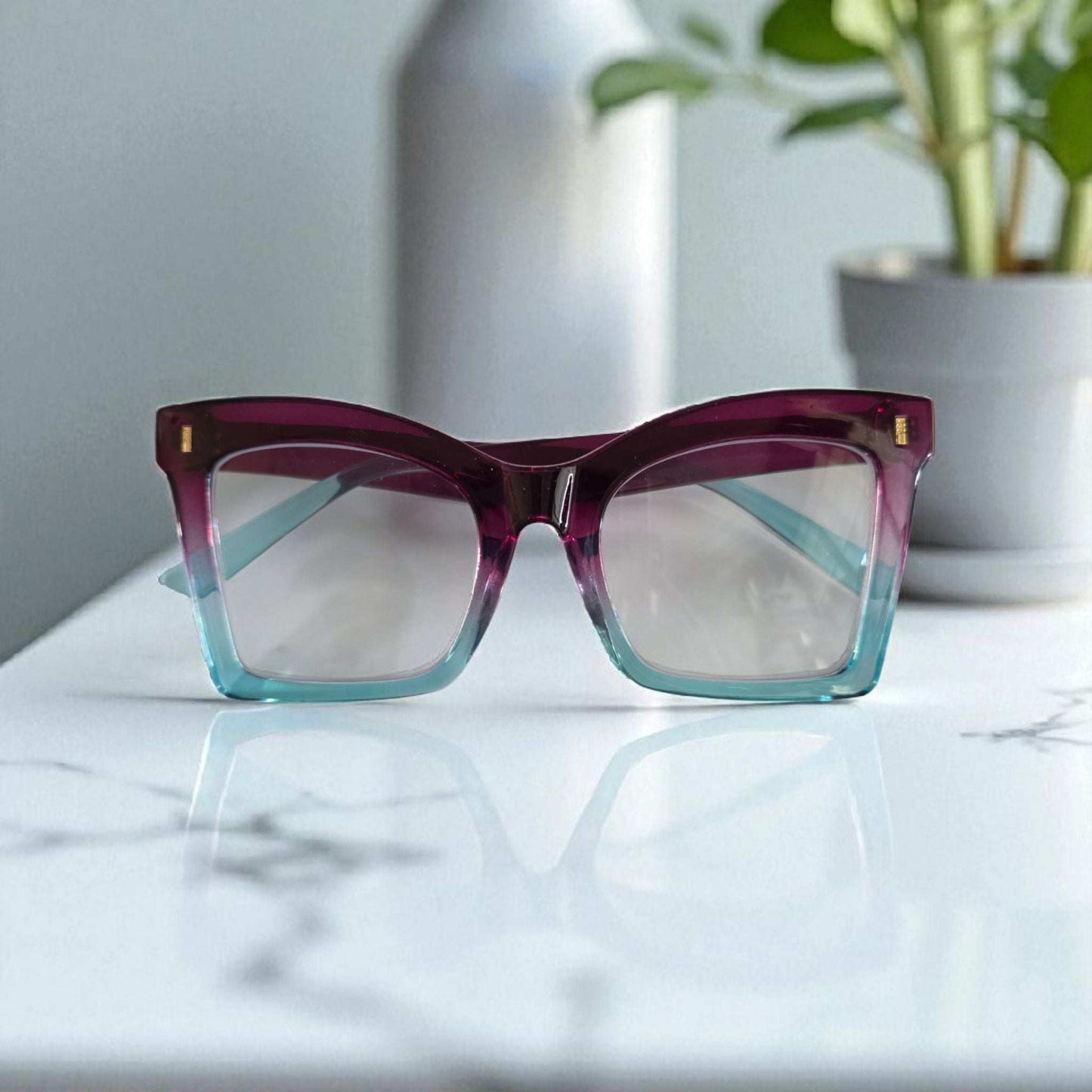 Square reading glasses with a purple upper frame fading into translucent blue at the bottom, featuring clear lenses and.