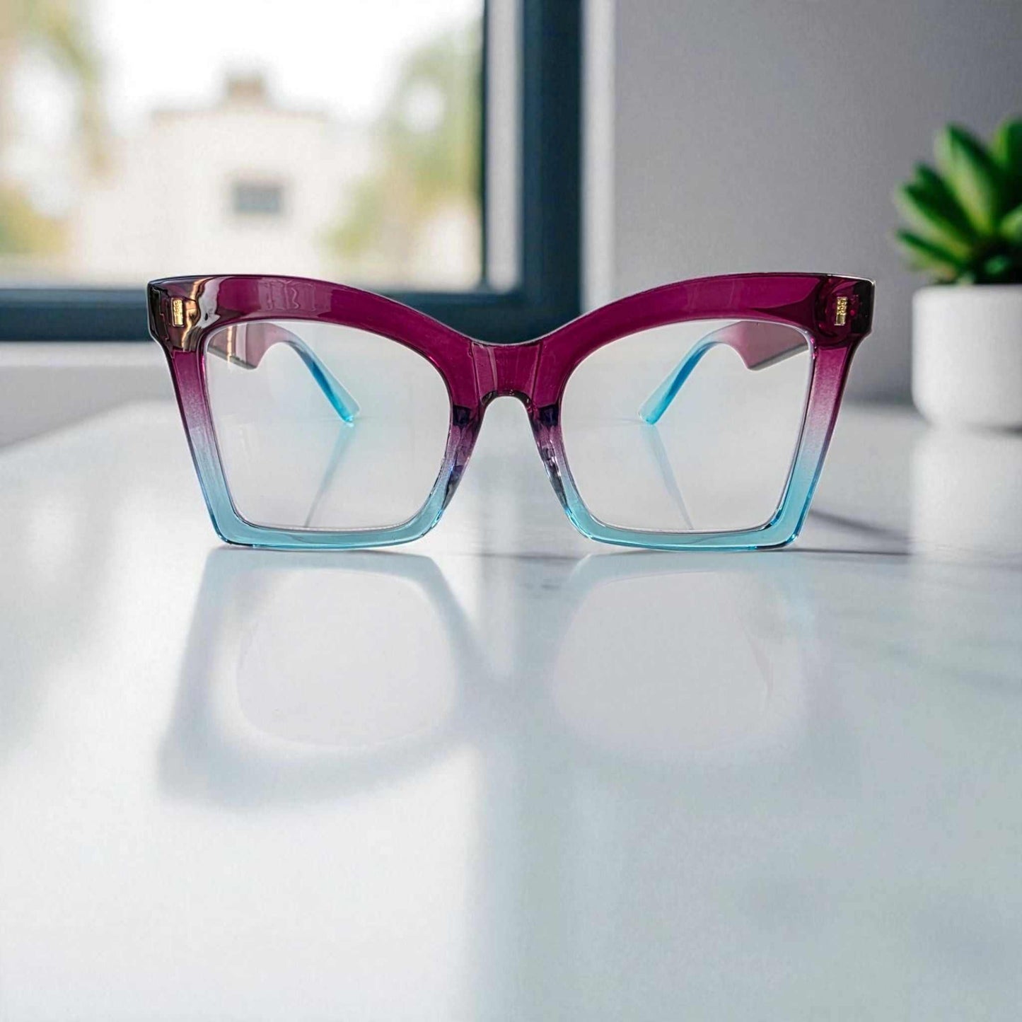 Purple and blue square reading glasses with blue light filter on a white surface near a window and plant