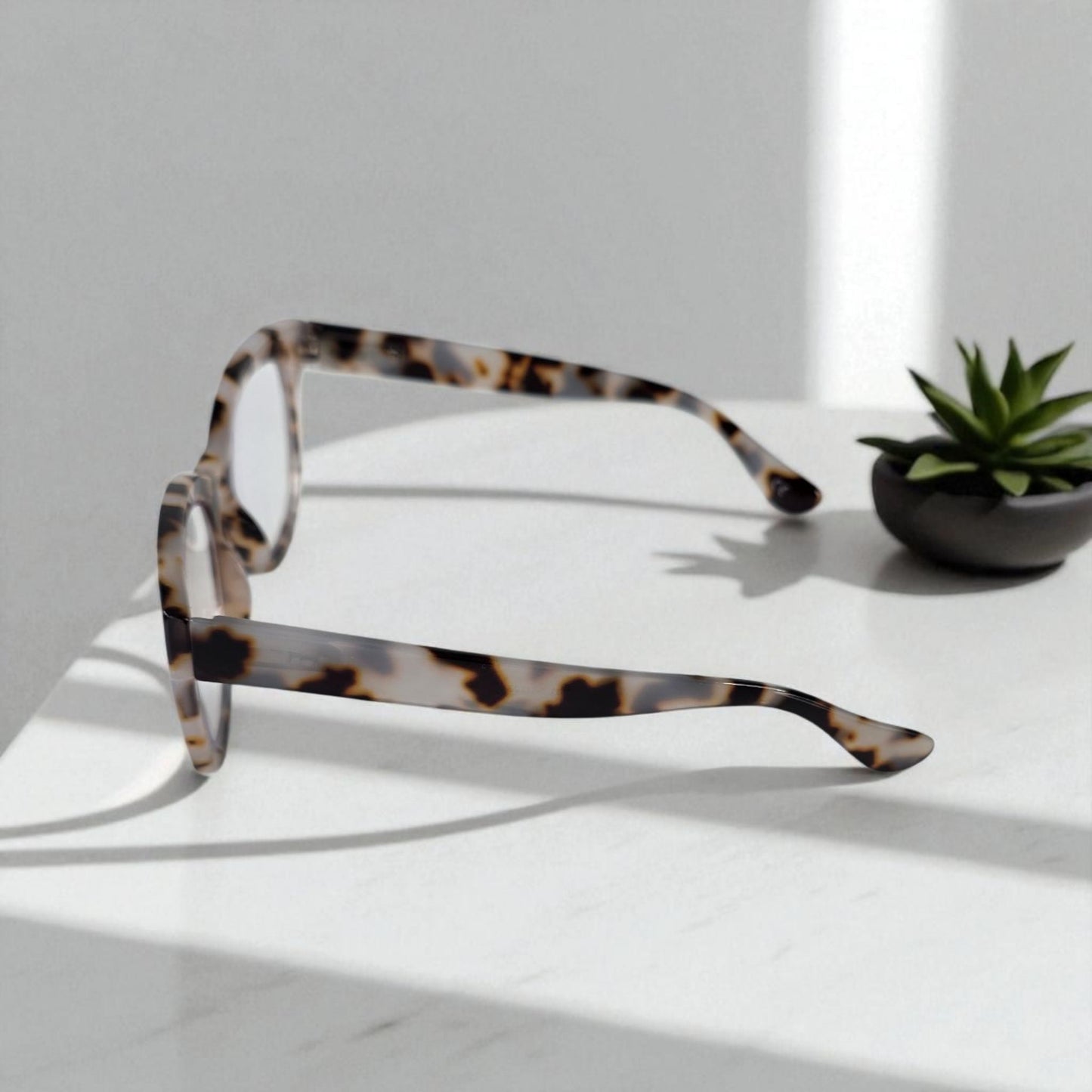 Creamy Ivory Tortoiseshell cat eye reading glasses with blue light filter on white surface next to small green succulent plant