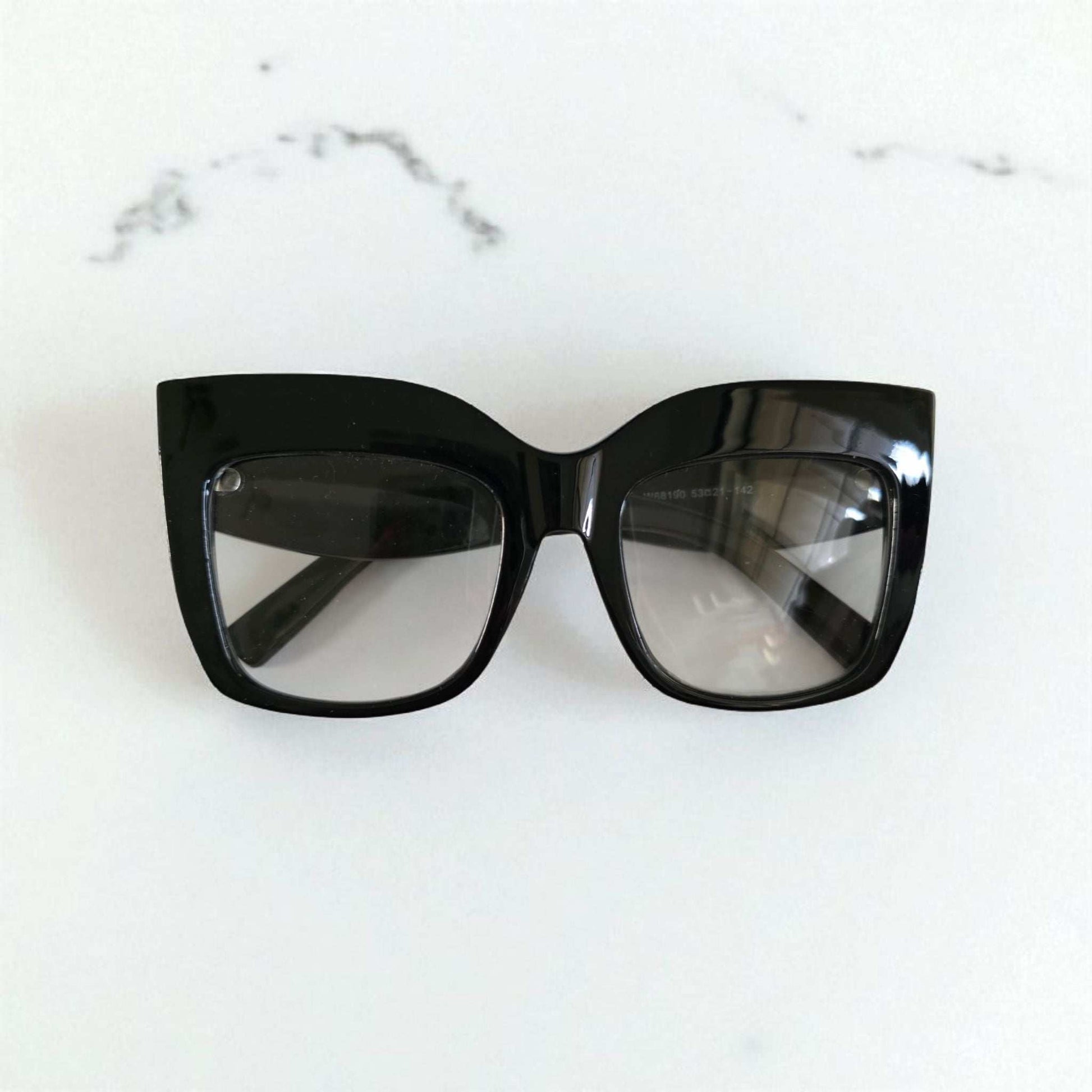 Black oversized cat eye reading glasses with thick glossy frames and slightly tinted lenses.