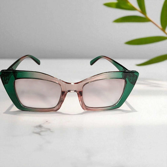 Antique pink and green blue light filter reading glasses with vintage cat-eye frame design on white surface with green leaves in background