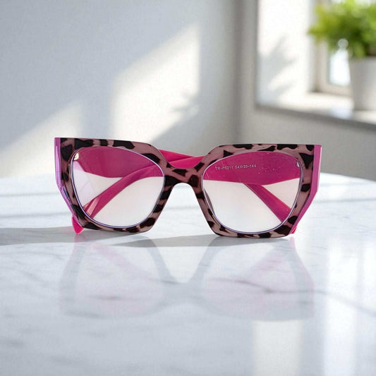 Pink and tortoiseshell reading glasses with blue light filter and square frames placed on a white surface in natural light