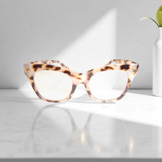 Ivory tortoiseshell reading glasses with blue light filter on white surface with sunlight and plant vase background